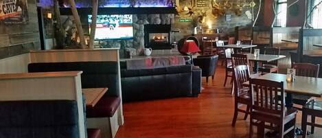 A cozy restaurant interior with a stone fireplace, wooden tables and chairs, and a television mounted on the wall.
