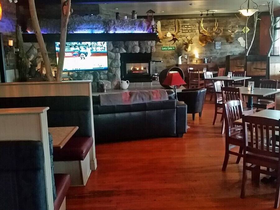 Un acogedor interior de restaurante con chimenea de piedra, mesas y sillas de madera, y un televisor montado en la pared.