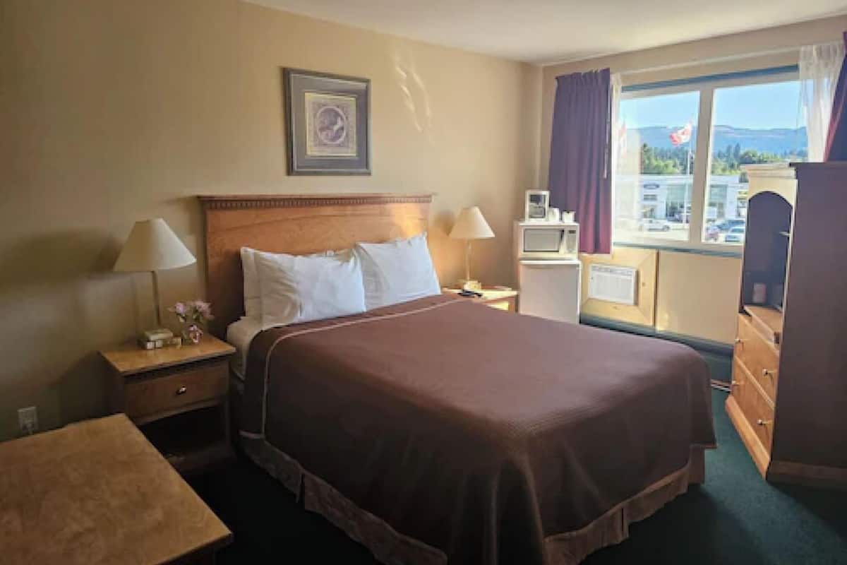 A hotel room with a large bed, two bedside tables, a dresser, a window with curtains, and a framed picture on the wall.