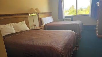 Une chambre d’hôtel avec deux lits, une table de chevet avec une lampe, une fenêtre donnant sur un paysage verdoyant et une moquette bleue.