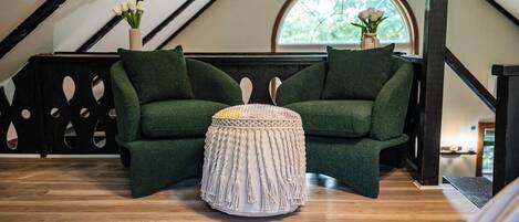 Una habitación acogedora con un sofá verde, un reposapiés redondo y una ventana con vistas a la vegetación.