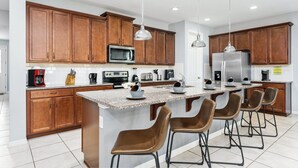 A modern kitchen with wooden cabinets, stainless steel appliances, and a central island with bar stools. - The Best Home's Resort Orlando (Kissimmee)