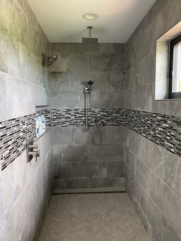 Ducha moderna con cabezal de ducha de mano y cabezal fijo, paredes de azulejos y una ventana.