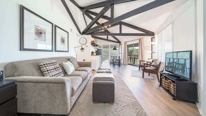A modern living room with a sofa, ottoman, and TV, a dining area, and a kitchen in the background. - Unique Octagon Home near Hot Springs (Hot Springs)