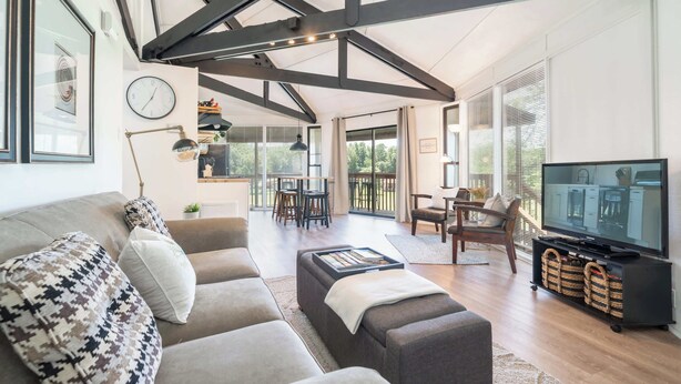 A modern living room with a sofa, ottoman, TV, and dining area. - Unique Octagon Home near Hot Springs (Hot Springs)