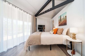 Un dormitorio con una cama, televisión, un cuadro y una lámpara.