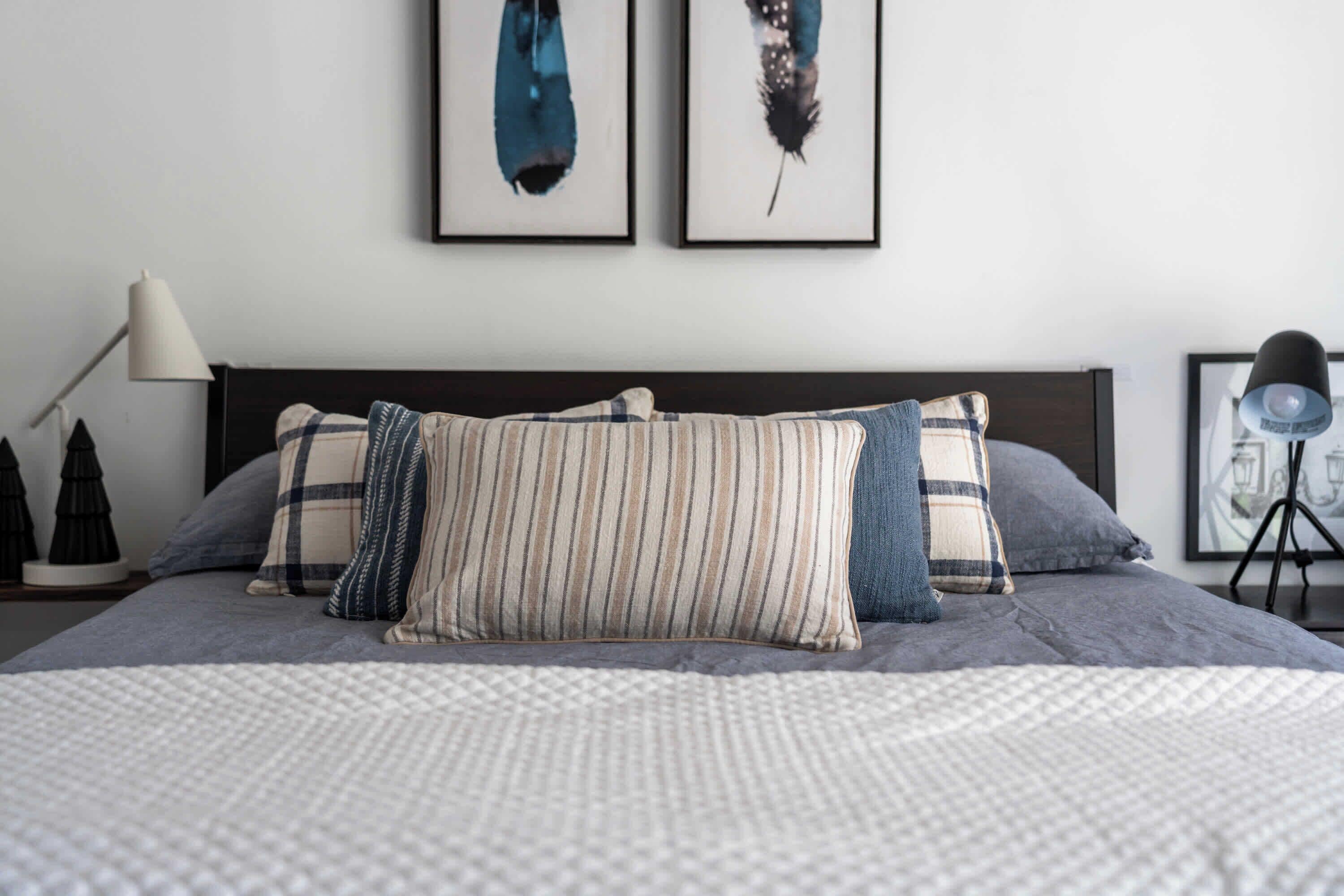 A neatly made bed with striped and solid pillows, a lamp, and framed artwork on the wall.