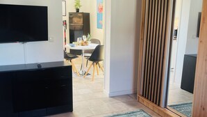 Een moderne slaapkamer met een groot bed, een aan de muur bevestigde televisie, een houten garderobe en een eethoek op de achtergrond.