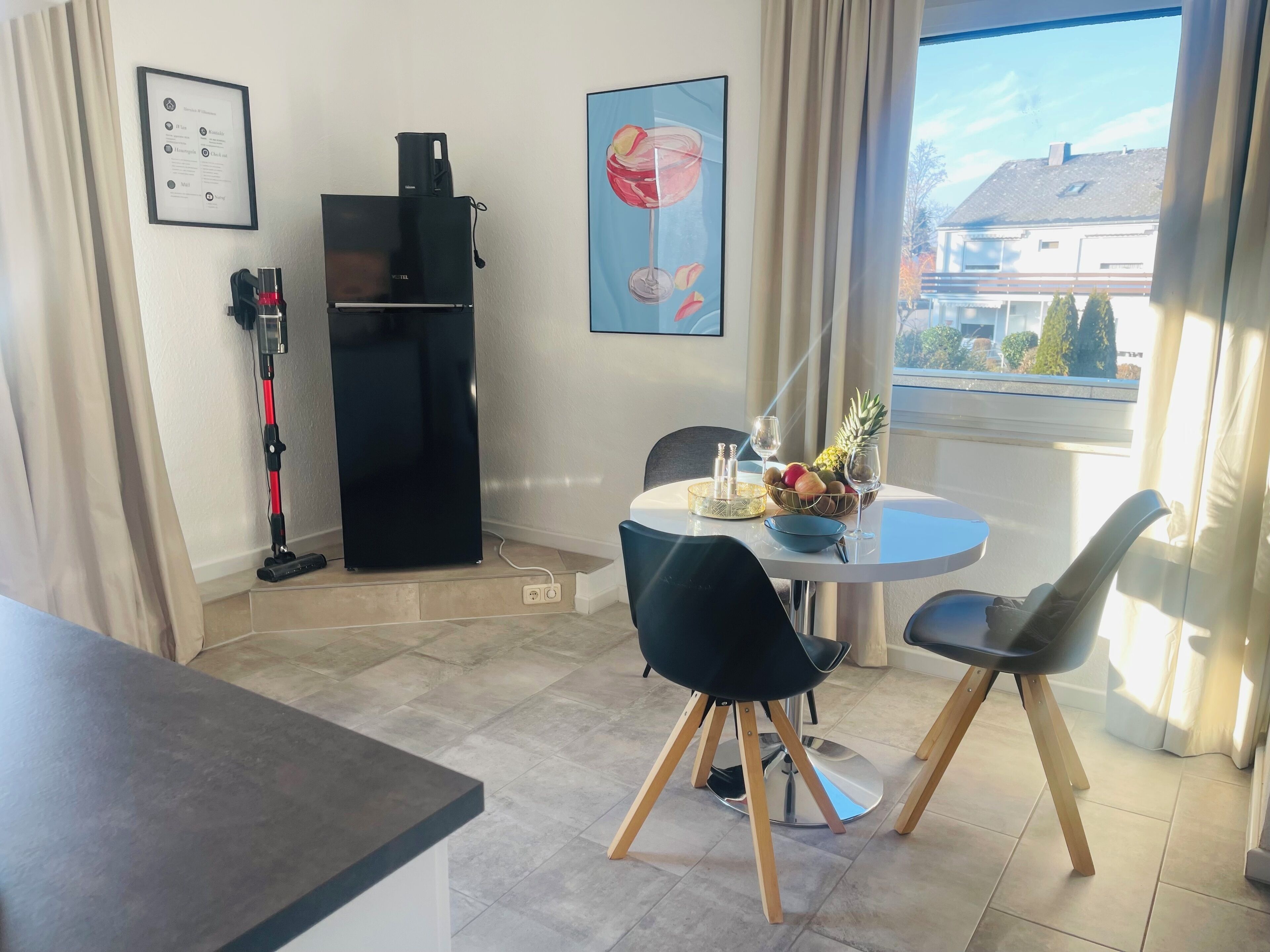 Un coin repas avec une table ronde, deux chaises, un panier de fruits et un tableau encadré accroché au mur.