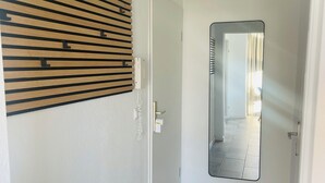 Een gang met een wand van houten latten, een witte deur en een spiegel die een kamer met gordijnen weerspiegelt.