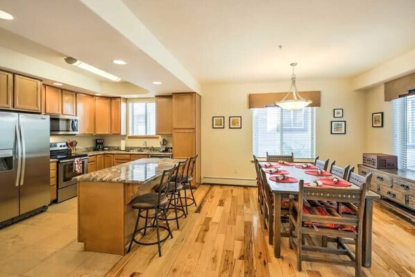 A modern kitchen with wooden cabinets, a central island, and a dining area with a table set for six. - Perfect Friends and Family Hideaway - Walk to town, Fantastic Location (Frisco)