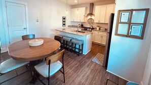 A modern kitchen with white cabinets, a central island with bar stools, a dining table with chairs, and a refrigerator. - Downtown Villa - steps from the heart of Waxhaw (Waxhaw)