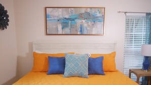 A bed with an orange quilt, two blue pillows, and a decorative pillow with a geometric pattern.