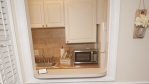 A kitchen with white cabinets, a microwave, and a small sink. There are two blue bar stools in front of the kitchen.