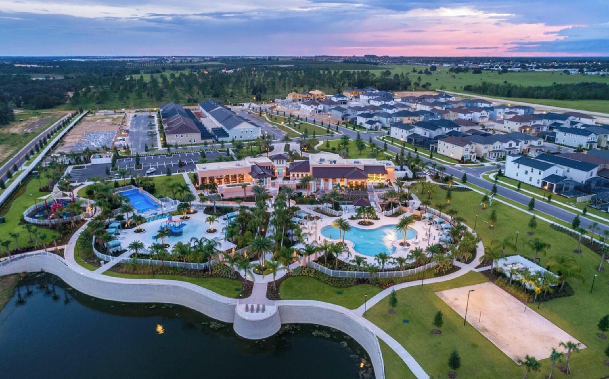 An aerial view of a residential area with a large swimming pool, multiple houses, and a well-maintained park area.