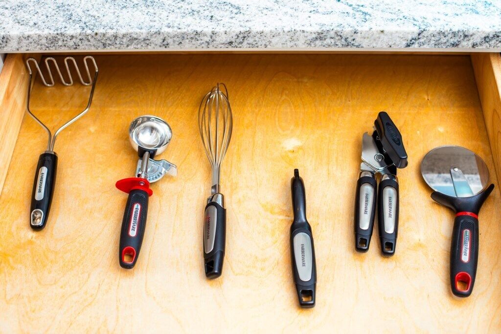 A drawer containing various kitchen utensils including a whisk, a grater, and a pair of scissors.