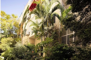 A building with multiple balconies, surrounded by dense foliage and trees.