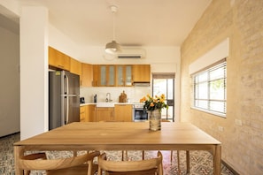 A modern kitchen with wooden cabinets, a stainless steel refrigerator, a dining table with chairs, and a vase with flowers. - Rustic Charm Hideaway • Balcony Oasis by SeaNRent (Tel Aviv-Yafo)