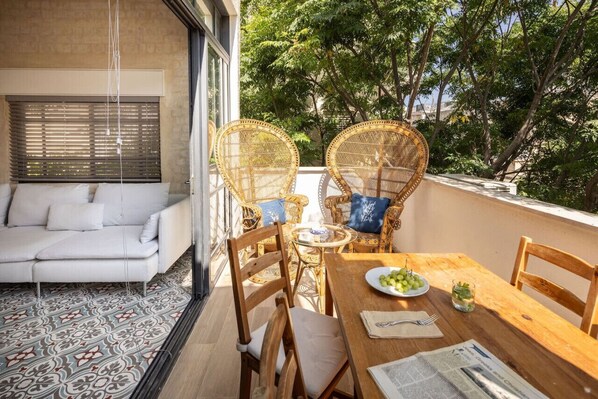 A balcony with wicker chairs, a wooden table, and a white sofa.