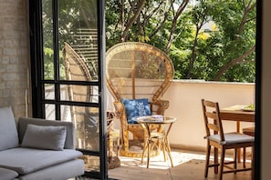 Une pièce comprenant un canapé, des fauteuils en osier, une table à manger et une vue sur les arbres, visible à travers une porte vitrée.