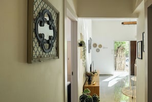 A hallway with a decorative mirror, a wooden bench with plants, and a door leading to another room.