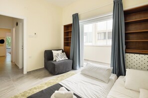 Un dormitorio con una cama, un sofá gris, un ventanal con cortinas y un cabecero de madera.