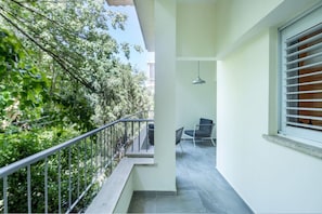 A balcony with a metal railing, a chair, a hanging light fixture, and a window with blinds.