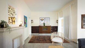 A living room with a fireplace, a wooden cabinet, a chair, and a sofa. - Your 2BR Green Oasis — Steps from Rabin Square (Tel Aviv)