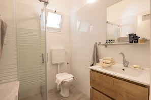 Un baño moderno con cabina de ducha de vidrio, inodoro, lavabo con espejo y tocador de madera.