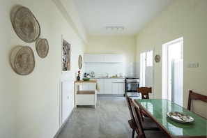 Una cocina moderna con armarios blancos, una mesa de comedor con sillas y adornos tejidos en la pared.