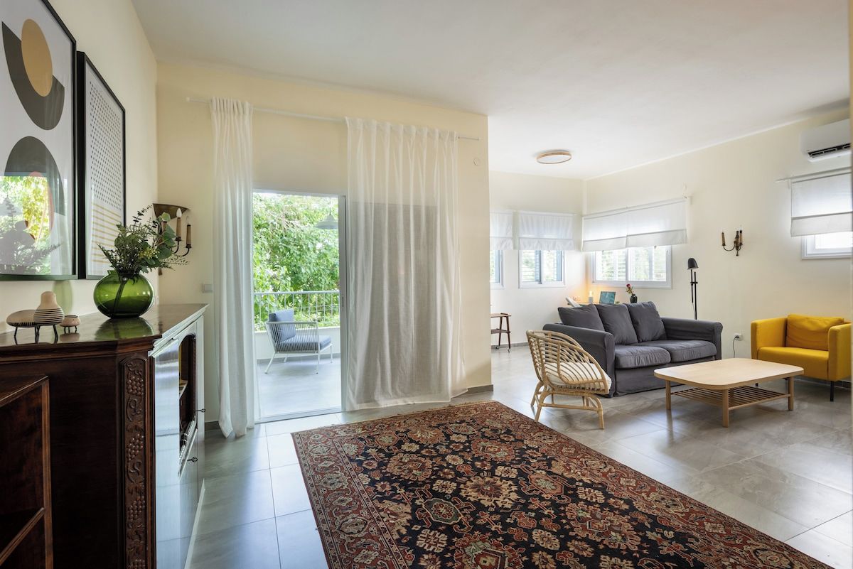 A spacious living room with a large rug, a sofa, a yellow armchair, and a dining table.