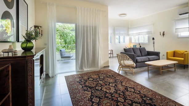 A spacious living room with a large rug, a sofa, a yellow armchair, and a dining table. - Your 2BR Green Oasis — Steps from Rabin Square (Tel Aviv)