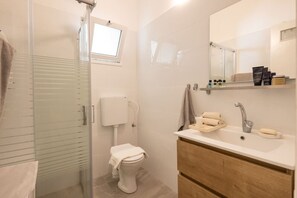 Un baño moderno con cabina de ducha de vidrio, inodoro, lavabo con tocador y espejo sobre el lavabo.