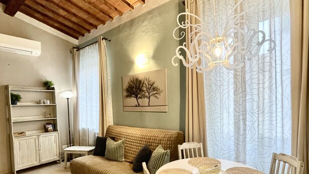 A cozy living room with a wooden ceiling, a sofa, a dining table with chairs, and a chandelier. - APARTMENT 'ORCHID' WHIT ONE BEDROOM.  (Firenze)