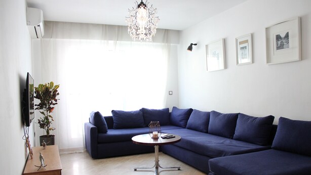 Un salon moderne avec un canapé d’angle, une petite table ronde et un lustre.