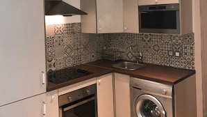 Une cuisine compacte dotée d’un four encastré, d’un micro-ondes et d’un lave-linge, avec un cr édence décorée de motifs et un plan de travail en bois.