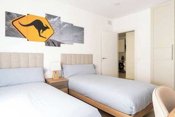 A hotel room with two beds, a nightstand, a wall-mounted kangaroo warning sign, and a view of the sky through the window.