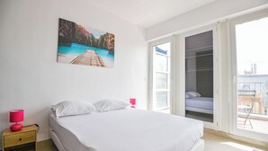 Une chambre à coucher avec un lit, une table de chevet, une fenêtre avec des stores et un tableau au mur.