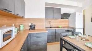 Une cuisine moderne avec des meubles gris, un plan de travail en bois, un four à micro-ondes encastré, une machine à café et un évier.