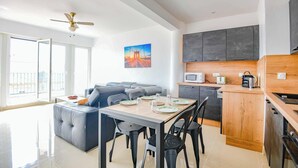 Un appartement moderne comprenant un coin repas, un canapé, une cuisine avec des meubles de couleur sombre et une grande fenêtre.