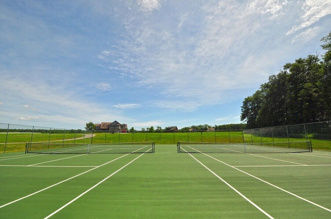 A tennis court with a net, surrounded by a fence, and a house in the background.