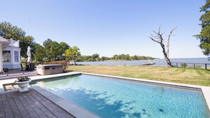 Une piscine rectangulaire avec une terrasse en bois, un jacuzzi et une vue sur un lac et des arbres.