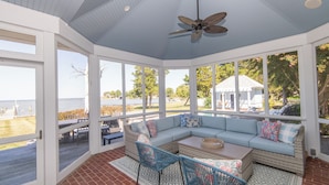Un espace extérieur abrité, doté d’un plafond bleu clair, d’un ventilateur de plafond et offrant une vue sur la plage.