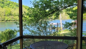 A covered outdoor seating area with a table and chairs, overlooking a lake with a dock and boat. - Newland's Cabin 5 (Baxter County)