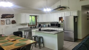 A modern kitchen with white cabinets, a granite countertop, stainless steel appliances, and a dining area with a wooden table and green placemats. - Newland's Cabin 5 (Baxter County)