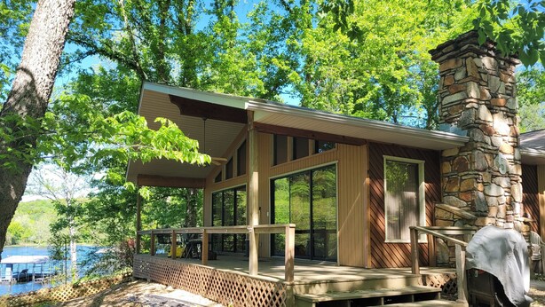 A modern cabin with a stone chimney, large windows, and a deck overlooking a lake. - Newland's Cabin 5 (Baxter County)