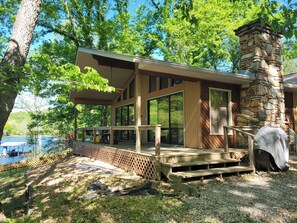 A modern cabin with a stone chimney, large windows, and a deck overlooking a lake. - Newland's Cabin 5 (Baxter County)