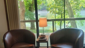 A room with two leather armchairs, a wooden coffee table, and a small table with a lamp and a bowl of cookies. Large windows offer a view of a lush green landscape. - Newland's Cabin 5 (Baxter County)