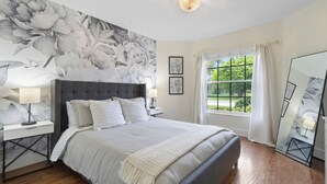A bedroom with a large bed, a nightstand with a lamp, a wall with a floral mural, a window with curtains, and a mirror. - Jupiter's Beacon Villa. Less than 2 miles from the beach in the heart of Jupiter (Jupiter)
