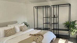 Quarto moderno com uma cama grande, um tapete tecido e uma estante de metal preta na parede.